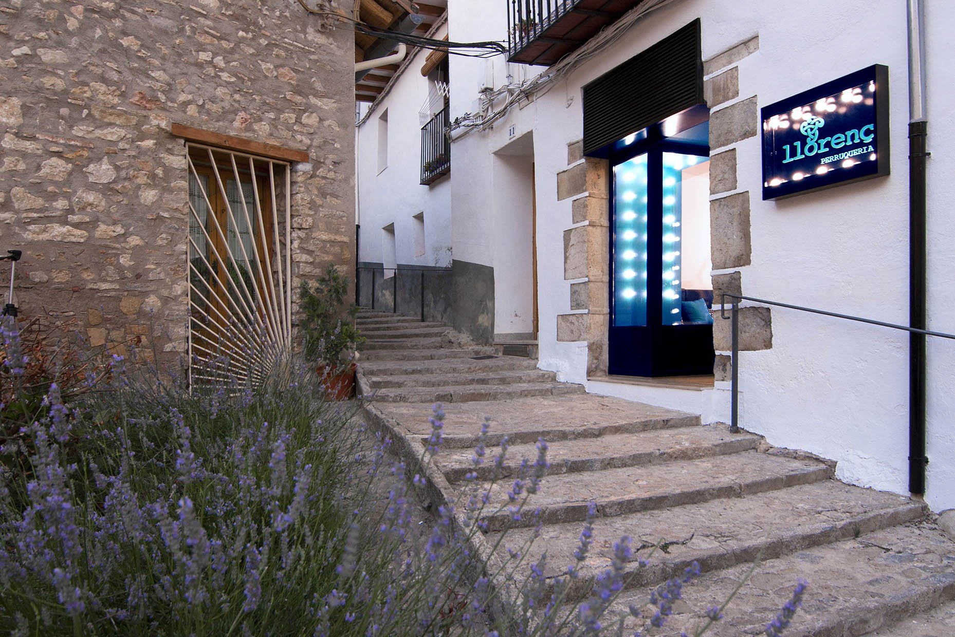 Fachada exterior peluquería. Entrada indicada mediante rótulo y pórtico iluminado con bombillas.