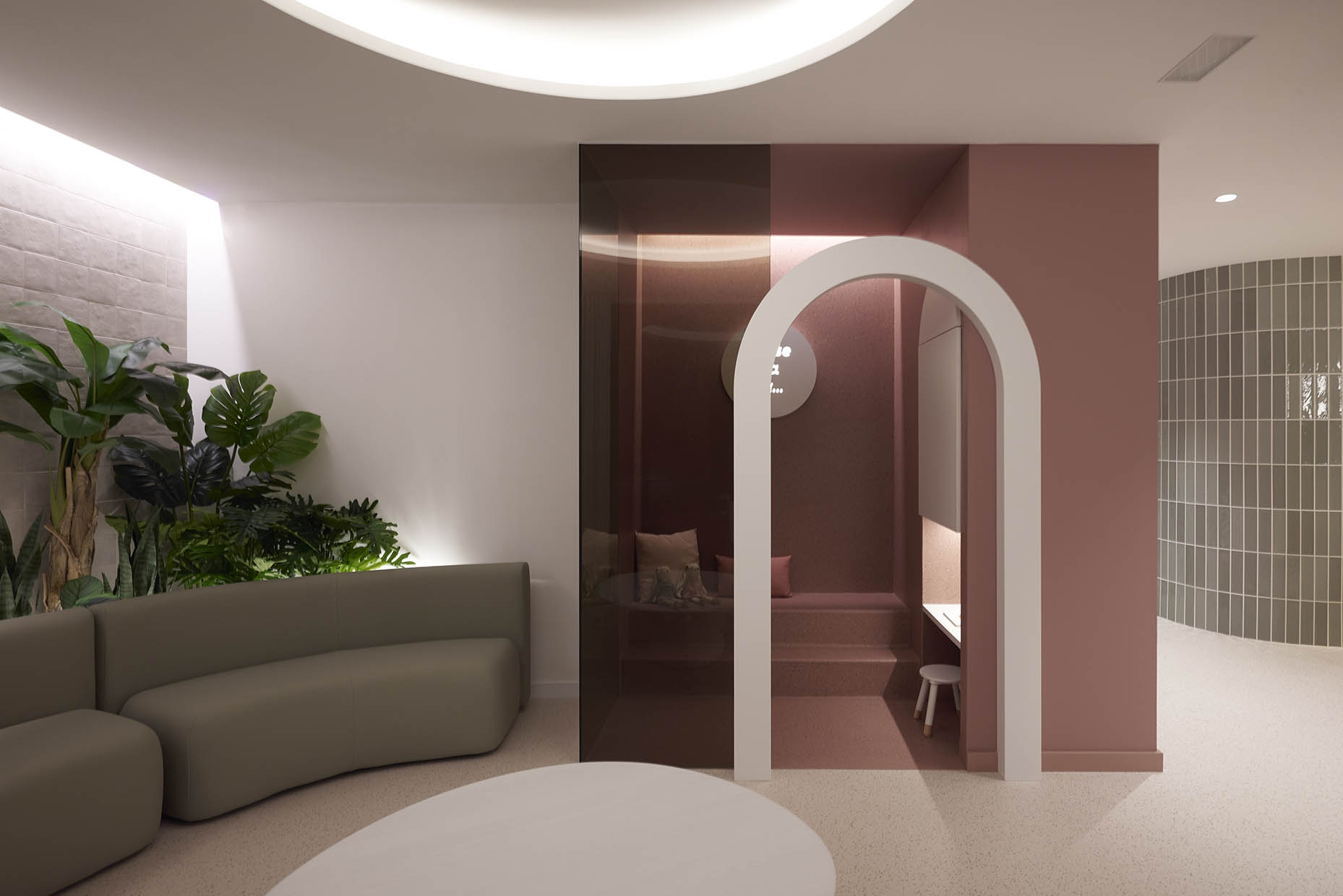 Espacio infantil dentro de la clínica con un diseño acogedor y envolvente. La entrada está enmarcada por un arco blanco que contrasta con las paredes en tonos rosados. En el interior, un banco empotrado con cojines y una pequeña mesa con taburete crean un ambiente ideal para los niños. La iluminación indirecta refuerza la sensación de calidez, mientras que un letrero iluminado con la frase ‘Érase una vez…’ sugiere un espacio lúdico y narrativo, evocando la imaginación y la tranquilidad.