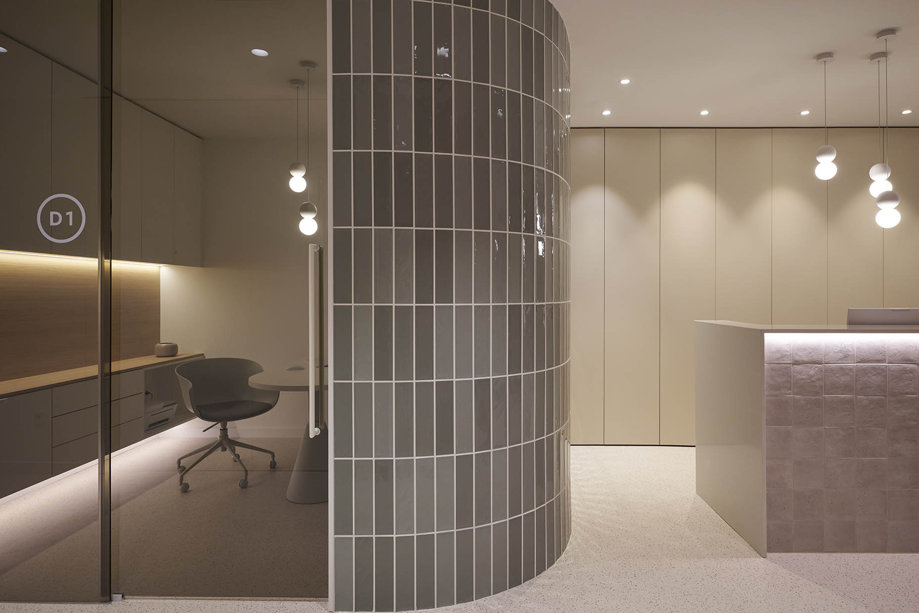 Despacho en una clínica con un diseño moderno y minimalista. La pared curva con azulejos en tono verde grisáceo crea una sensación envolvente y sofisticada