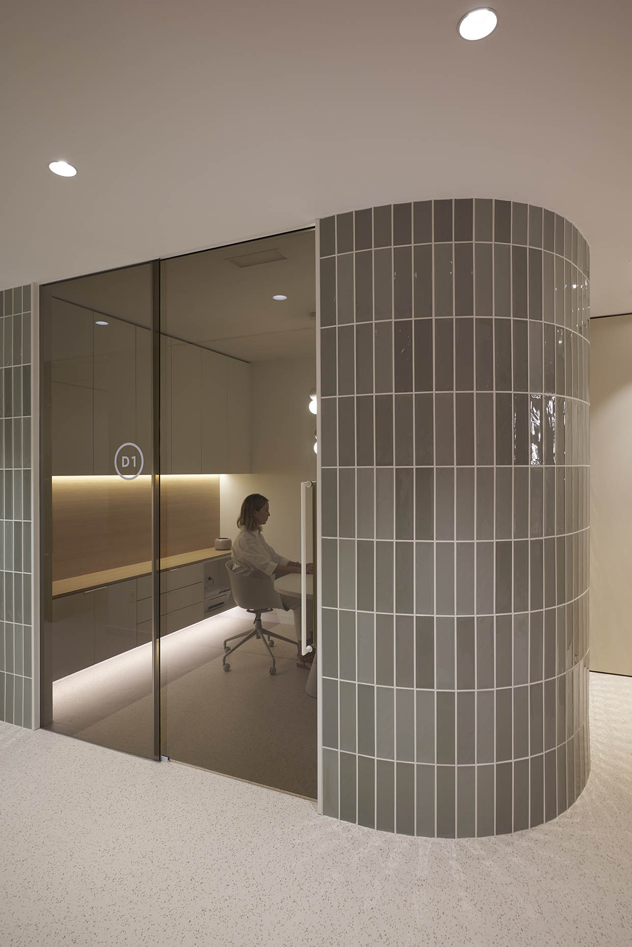 Despacho en una clínica con un diseño moderno y minimalista. La pared curva con azulejos en tono verde grisáceo crea una sensación envolvente y sofisticada