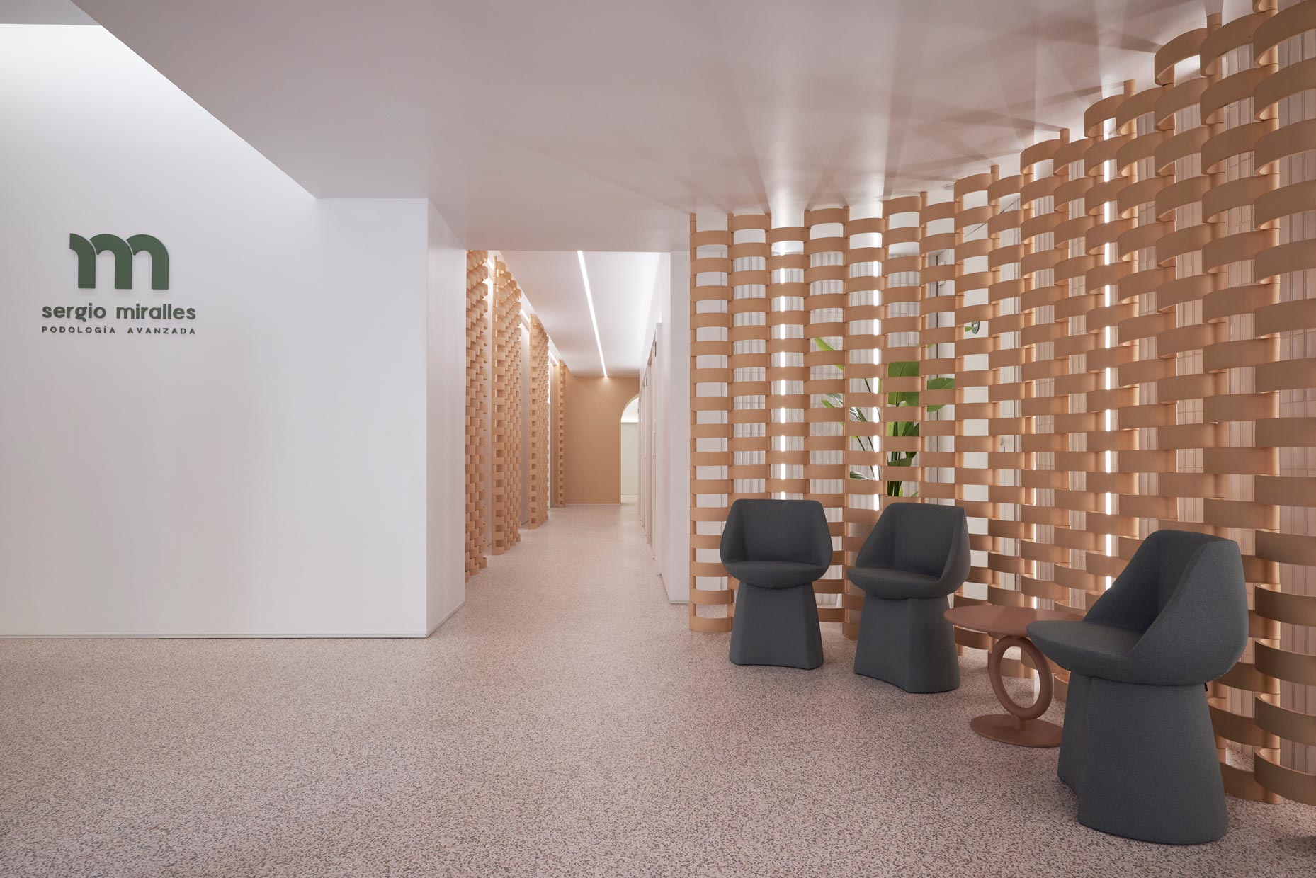 Zona espera y pasillo de diseño moderno y minimalista, celosías, mobiliario verde y luz indirecta que aporta calidez al espacio